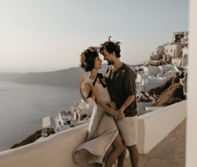 portrait-couple-background-greek-city-brunette-lady-beige-dress-man-stylish-outfit-looks-each-other-with-love-sea-background